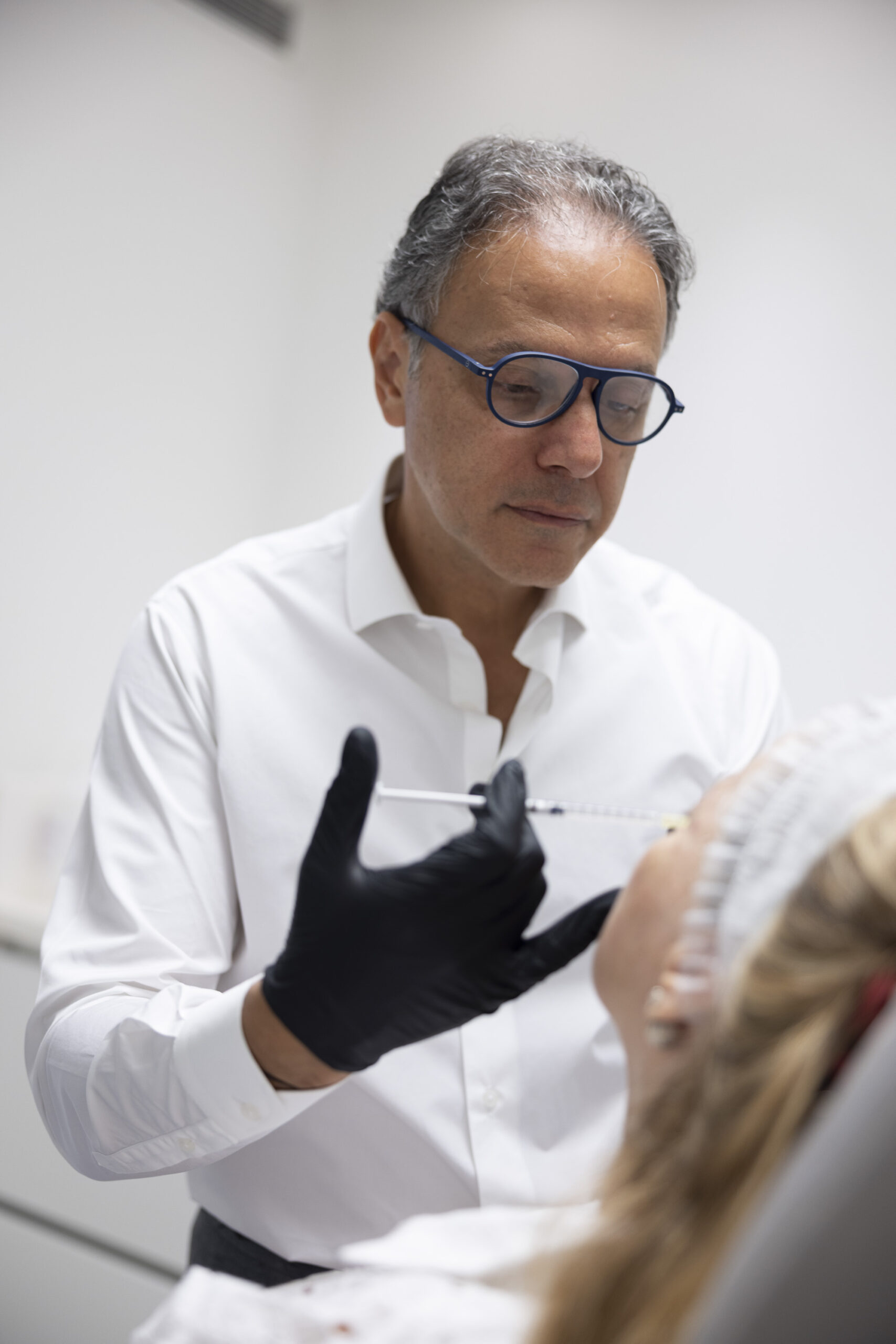 Dr. Dany Touma injecting fillers into a female patient's face at a cosmetic clinic